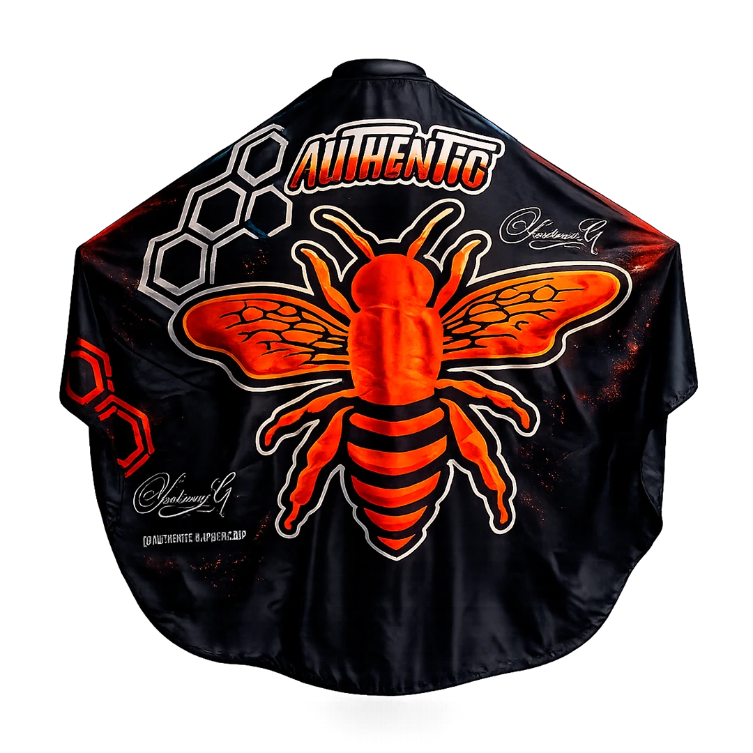 Capa de barbería Authentic Vision Imperial, tela profesional antifluidos negra con gráfico de abeja en naranja fuego y detalles geométricos.